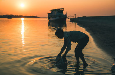 Side view of man holding plastic at beach during sunset