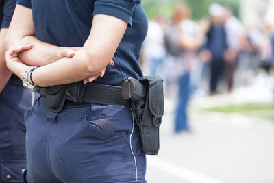 Midsection of police officer standing with hands behind back on street