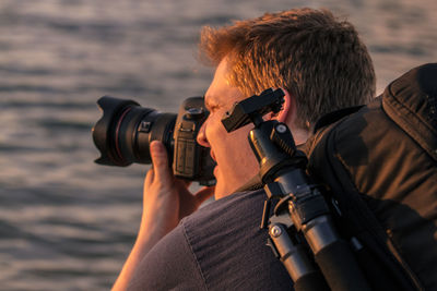 Rear view of man photographing through camera against sea