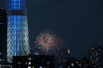 Low angle view of illuminated fireworks against buildings at night