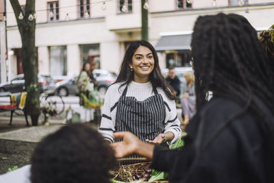 Smiling female vendor talking with customer doing shopping at farmer's market