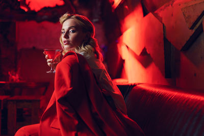 Portrait of young woman holding cocktail while sitting in nightclub