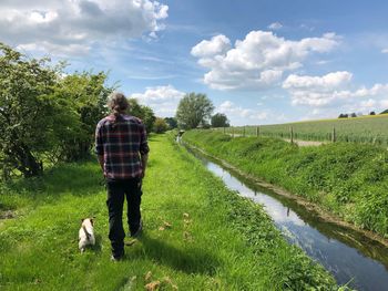 Rear view of person with dog on grass against sky