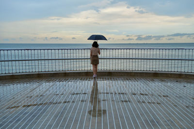 Rear view of woman walking on pier over sea against sky
