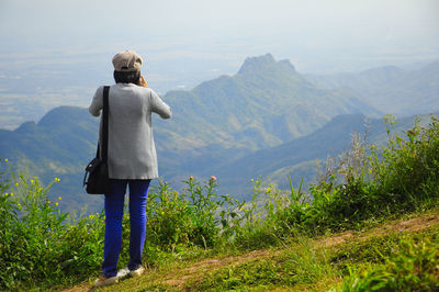 Rear view of woman standing on mountain against sky