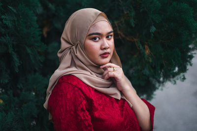 Portrait of beautiful young woman standing against plants