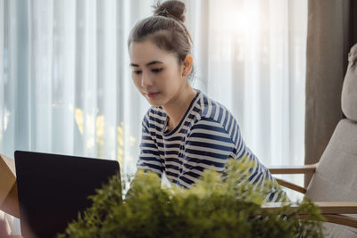 Side view of young woman using laptop at home