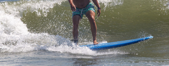 Side view of a man riding his blue surfboard surfing at gilgo beach on long island.