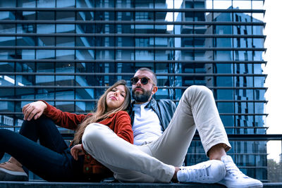 Young couple sitting on bench against building