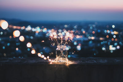 Sparklers in bottle against illuminated city during sunset