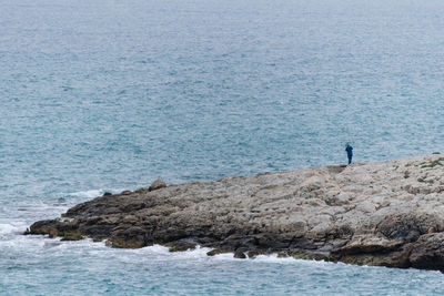 Mid distance view of man on rock by sea