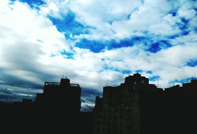 Low angle view of silhouette buildings against cloudy sky