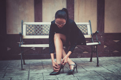 Mid adult woman adjusting sandal while sitting on bench