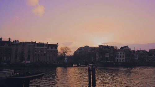 Buildings by river against sky during sunset