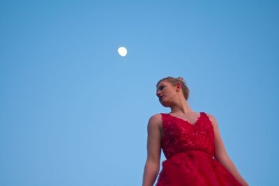 Low angle view of young woman against clear blue sky