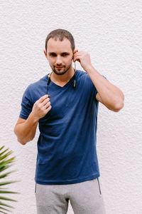 Smiling man listening musing while standing against wall outdoors