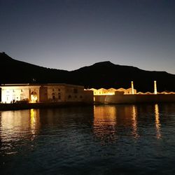 Silhouette buildings by lake against clear sky