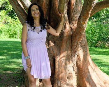 Young woman standing by tree trunk