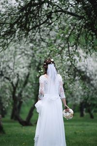 Rear view of bride standing against trees on field