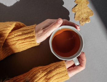 The hands of a woman dressed in a wool sweater on a cold day and holding a cup of warm tea 