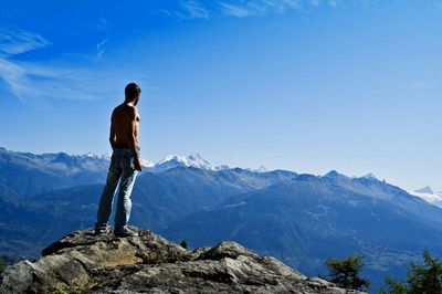 Rear view of shirtless man standing on mountain against sky