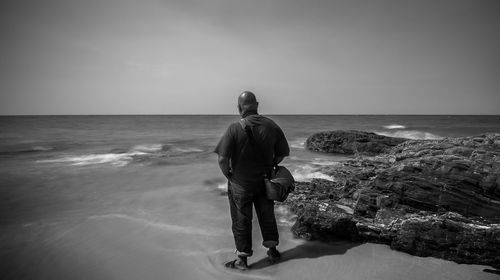 Rear view of man standing at beach against clear sky