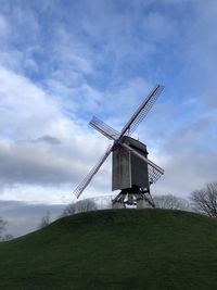 Low angle view of traditional windmill on field against sky