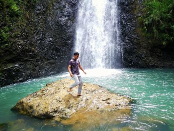 Full length of woman standing on rock at waterfall