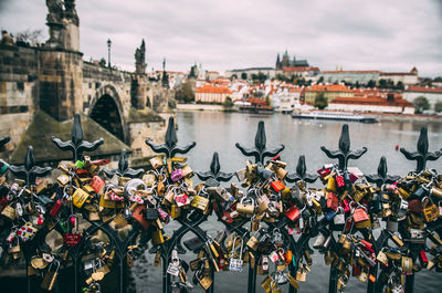 Close-up of padlocks on bridge over river against cloudy sky in city