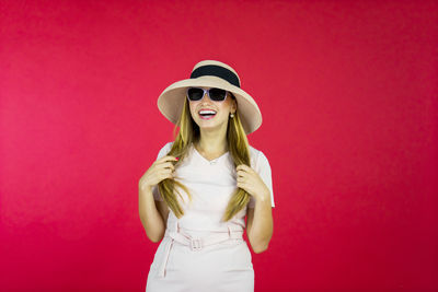 Young woman wearing sunglasses standing against red background