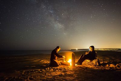 Young couple sitting on beach against sky at night