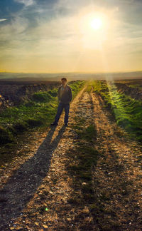 Man standing on dirt road against sky during sunset