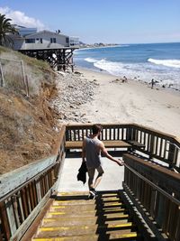 Rear view of man walking on steps at beach against sky