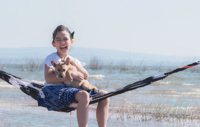 Girl with dog sitting on hammock against sky