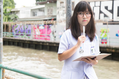 Thoughtful female doctor holding book while standing outdoors