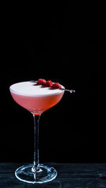 A glass of pink raspberry cocktail on a black background