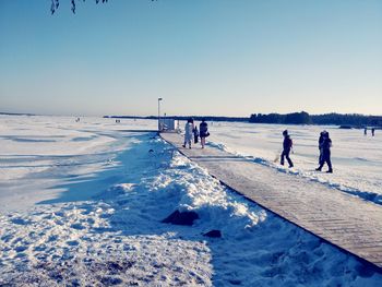 People walking on boardwalk amidst snow covered landscape against sky