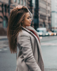 Young woman looking away while standing on street in city