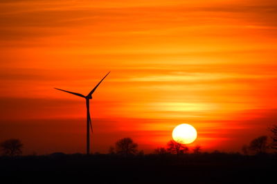 Silhouette wind turbines on landscape against romantic sky at sunset