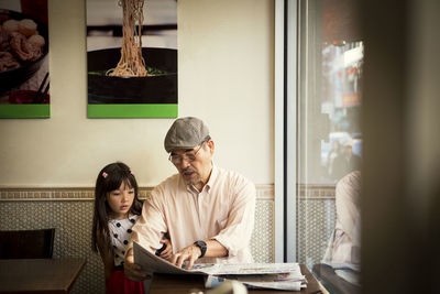 Grandfather showing newspaper while sitting with granddaughter in restaurant