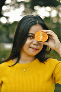 Outdoor lifestyle, beautiful girl wearing a yellow dress holding an orange, covering one eye