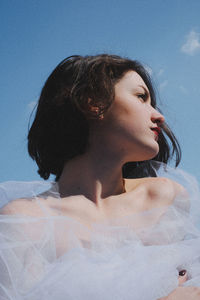 Low angle view of young woman in white dress against sky
