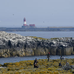 People on rocks by sea against sky