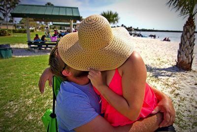 Couple kissing while sitting at beach against sky