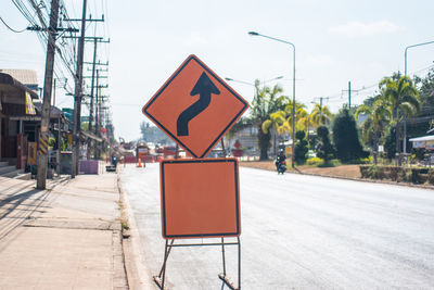 Road sign on street in city against sky