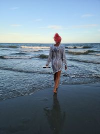 Rear view of woman walking at beach against sky