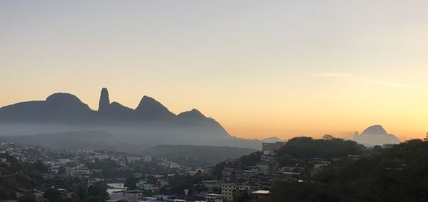 Silhouette buildings in city against clear sky during sunset