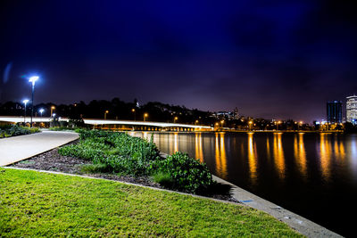 Illuminated city by river against sky at night