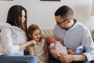 Happy family of four with the new newborn baby. older sister, father and mother in the sofa