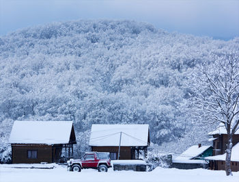 Red suv car in the snow near a wooden house on a background of forest hills in the winter time